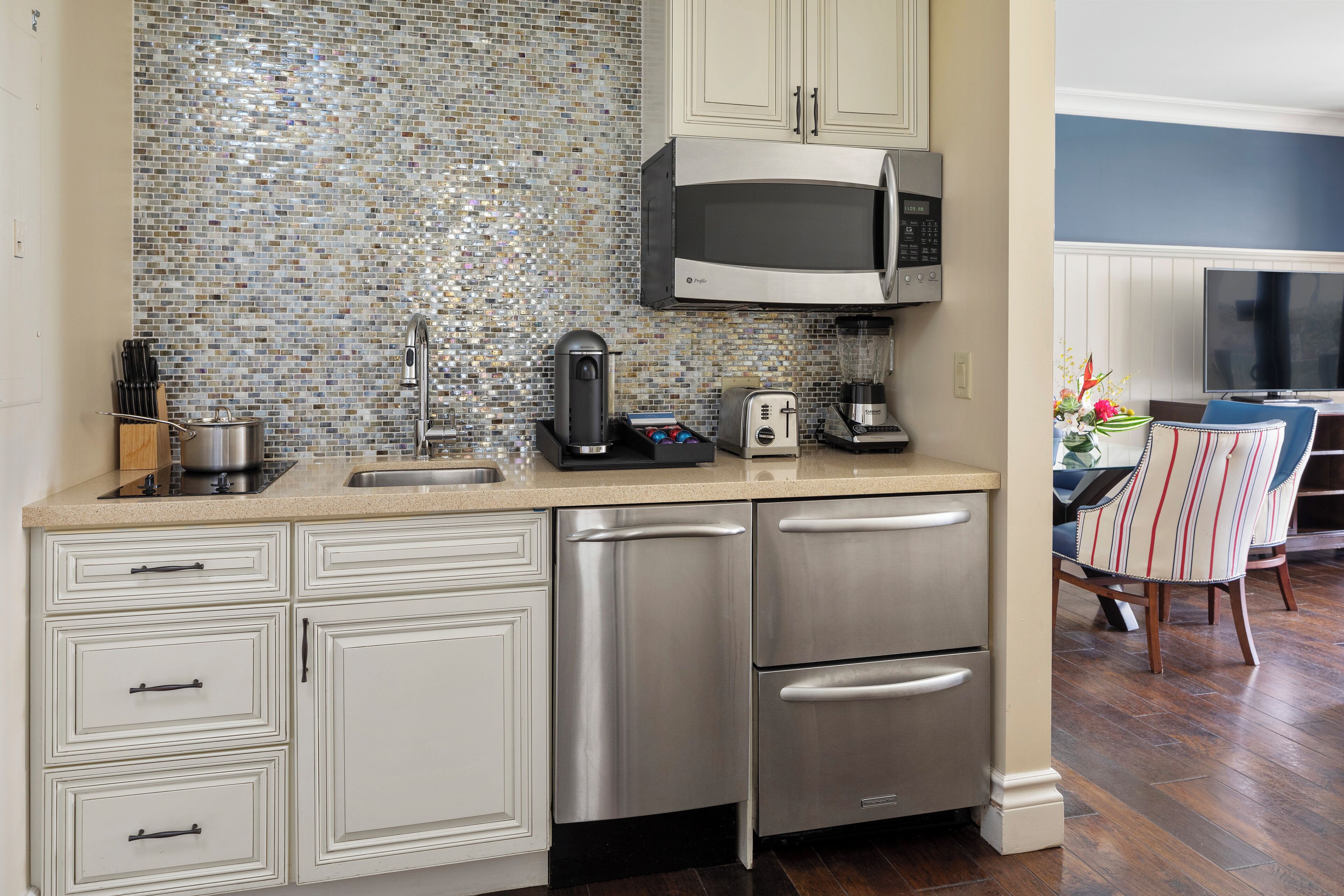 A kitchen with a stainless steel microwave, a coffee maker, and a toaster. There is a sink and a cabinet with drawers.