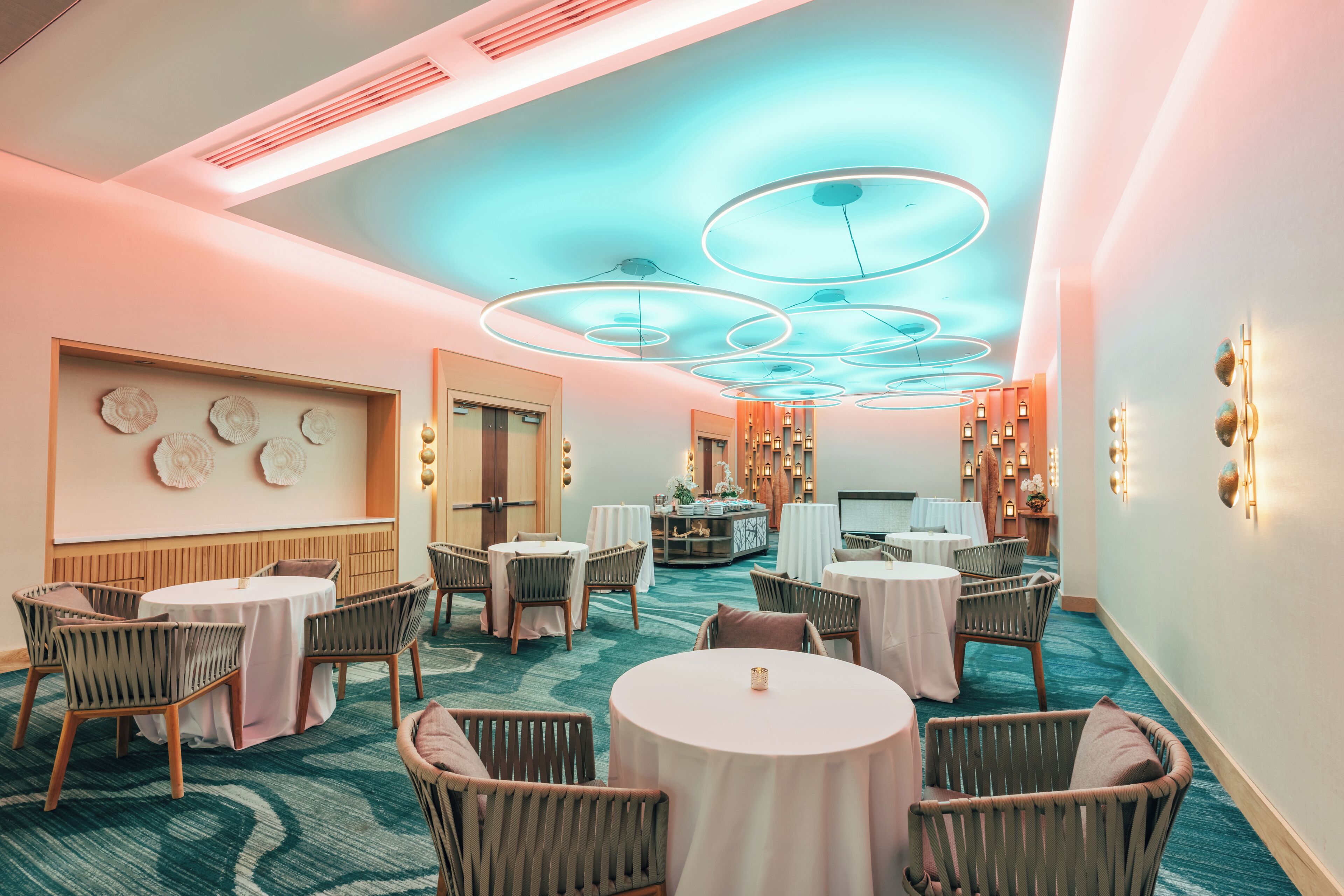 A hotel lobby with round tables, wicker chairs, and a central bar area.