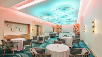 Un hall d’hôtel avec des tables rondes, des chaises en osier et un bar central.