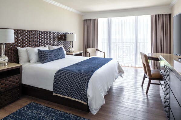 A hotel room with a large bed, a desk, a chair, a TV, and a balcony with curtains. - Opal Grand Oceanfront Resort & Spa (Delray Beach)