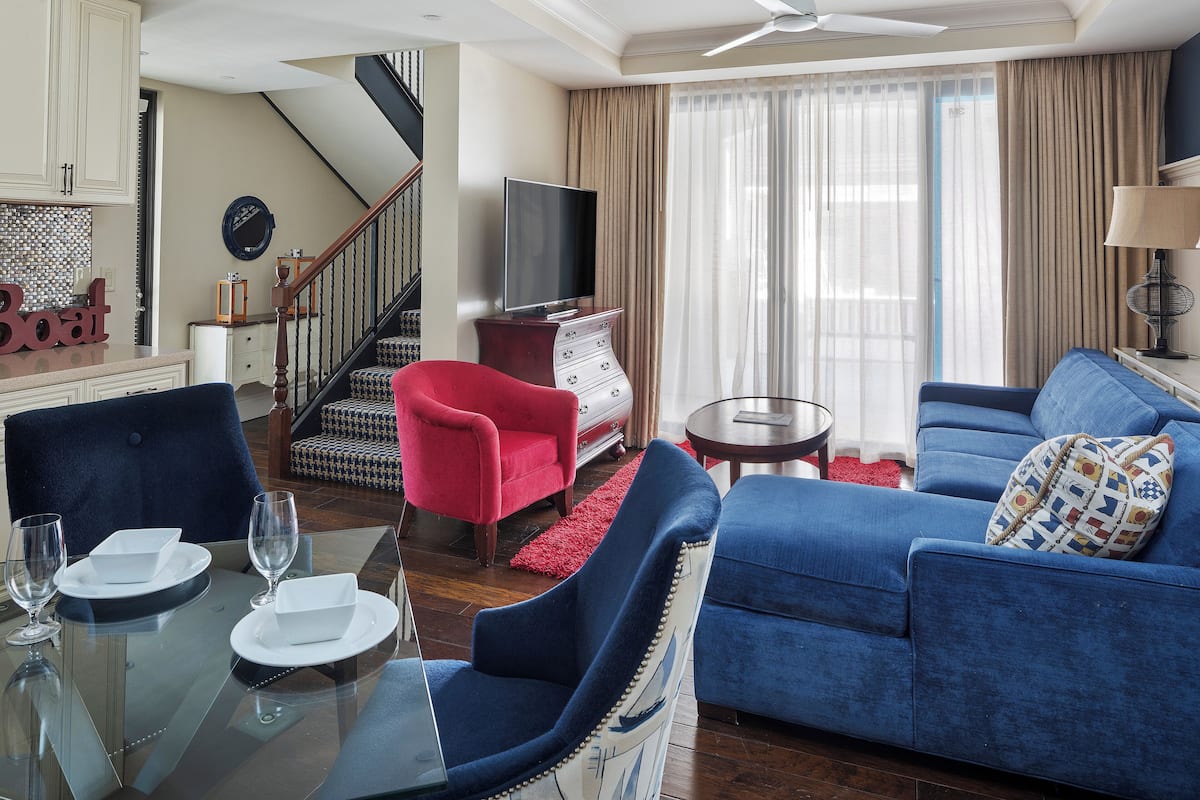 Un salón moderno con un sofá azul, un sillón rojo y una mesa de comedor de cristal para dos personas.