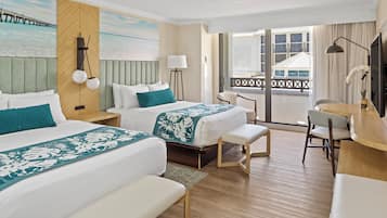A hotel room with two beds, a desk, a chair, and a view of a building through large windows.