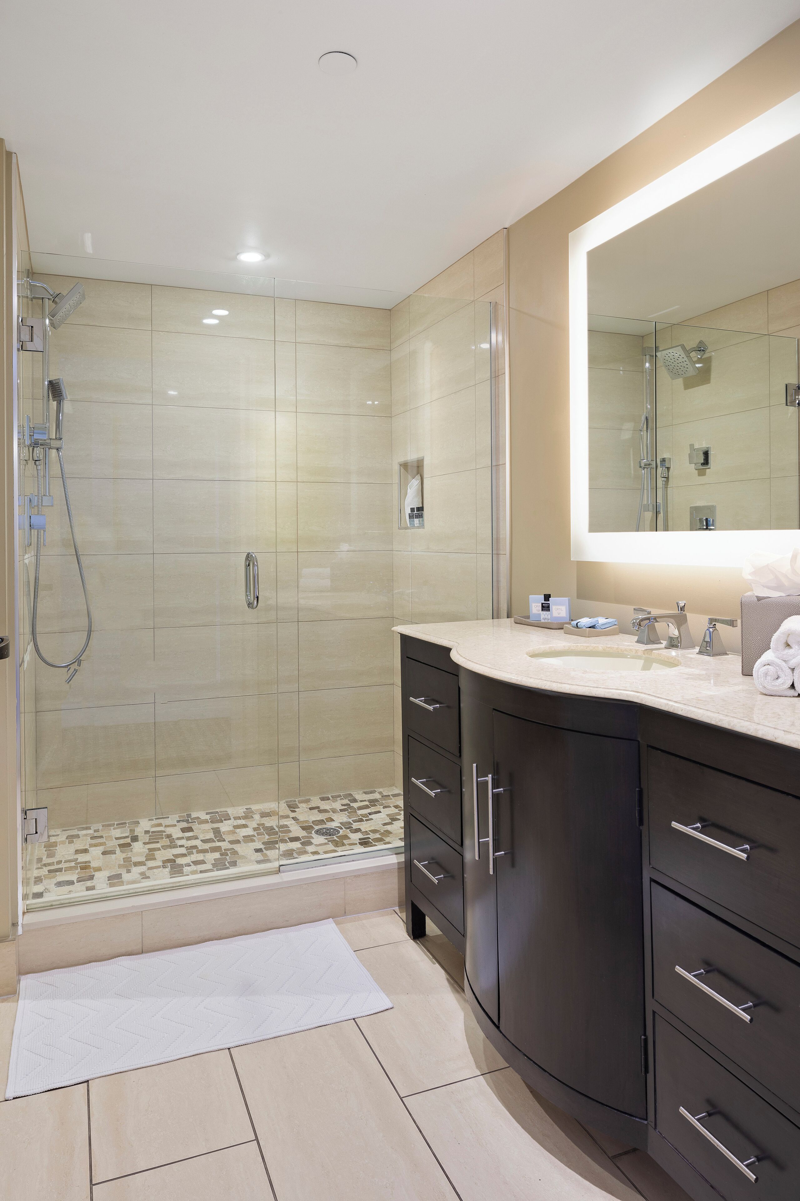A modern bathroom with a glass-enclosed shower, a large mirror, and dark cabinetry.