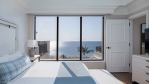 A bedroom with a large window overlooking the sea, a bed with a blue-striped bedspread, a bedside table with a lamp, and a TV on a dresser. - Opal Grand Oceanfront Resort & Spa (Delray Beach)
