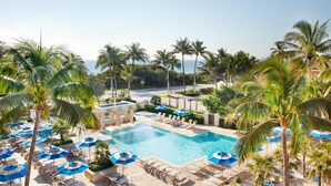 A pool area with lounge chairs and umbrellas, surrounded by palm trees and a view of the ocean. - Opal Grand Oceanfront Resort & Spa (Delray Beach)