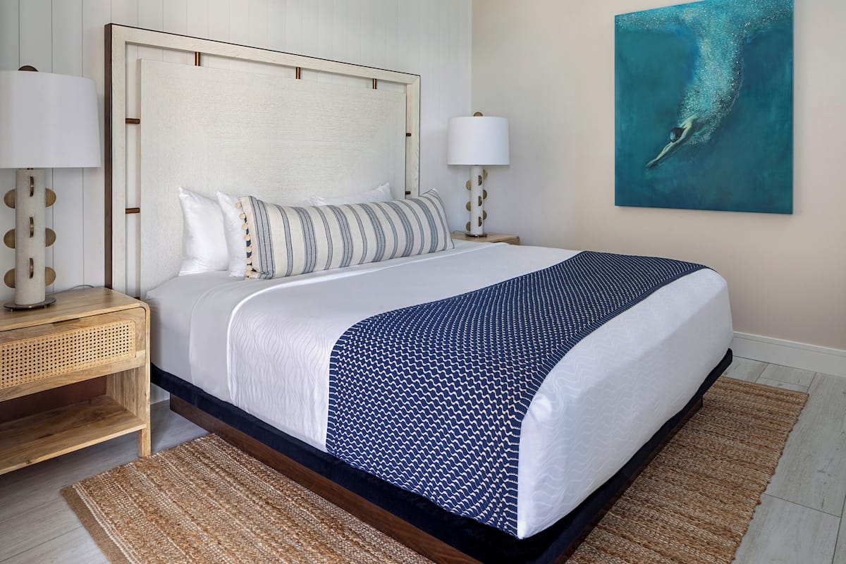 Una cama bien hecha con un cojín a rayas, una manta estampada en azul y una mesita de noche con una lámpara.