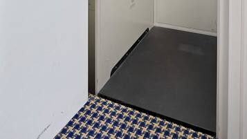 A narrow hallway with a metal door, a control panel, and a small window.