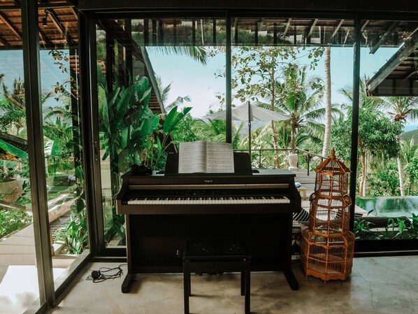 A piano with sheet music on a balcony with a view of palm trees and a birdcage.