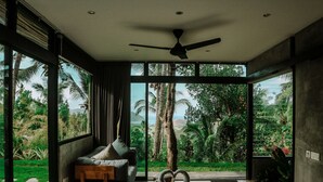A modern bedroom with a large bed, a ceiling fan, and a view of a tropical landscape.