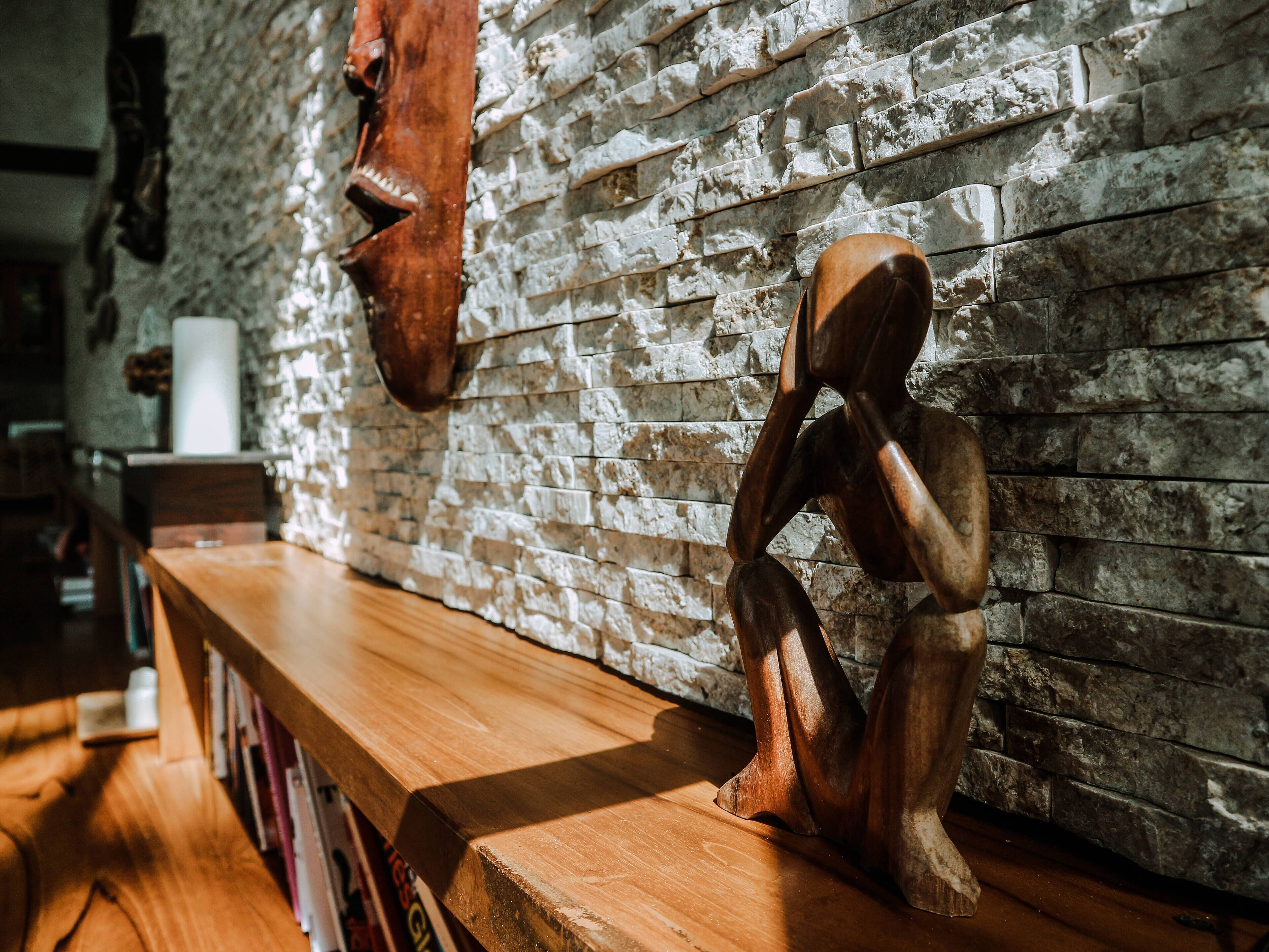 A wooden bench with books, a brick wall, and a wooden sculpture.