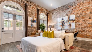 A bedroom with a brick wall, a large bed with white bedding, a sofa, and a large abstract painting. - Luxury Condo Walk Anywhere & Everywhere! The Bordeaux (New Orleans)