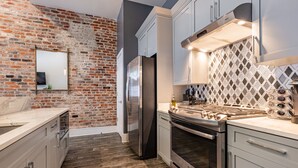 A modern kitchen with a brick wall, stainless steel appliances, and a patterned backsplash. - Luxury Condo Walk Anywhere & Everywhere! The Bordeaux (New Orleans)