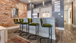 A modern kitchen with a brick wall, white cabinets, and a bar area with green cushioned stools. - Luxury Condo Walk Anywhere & Everywhere! The Bordeaux (New Orleans)