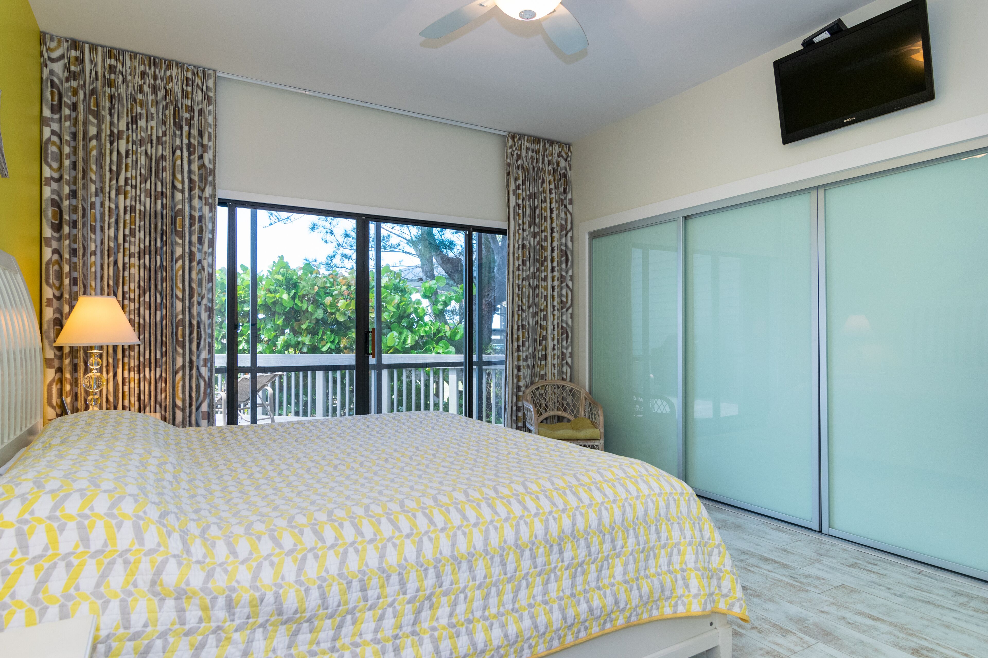 Un dormitorio con una cama grande, ventilador de techo, televisión y puerta corrediza al exterior.