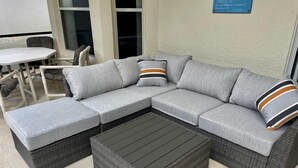 Un canapé modulable avec des coussins gris et des oreillers à rayures, une table basse en bois foncé à motifs tissés, et une petite table à manger avec des chaises.