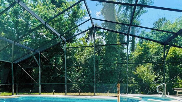Une piscine entourée d’arbres et dotée d’une paroi en verre.