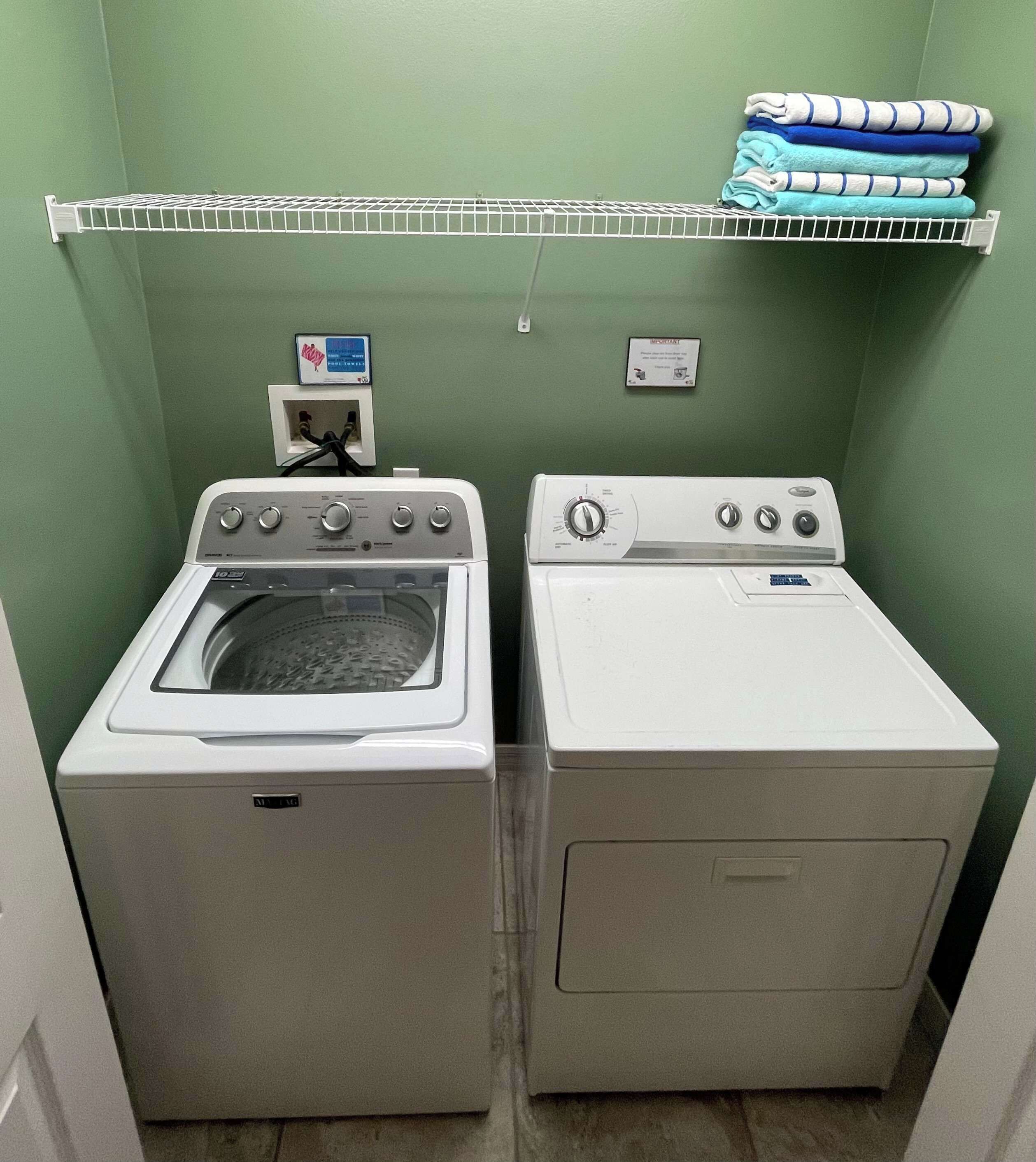Une buanderie équipée de deux machines à laver et deux sèche-linge superposés, d’une étagère en métal où sont pliées des serviettes, et d’une prise de courant.