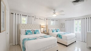 Un dormitorio con dos camas, ropa de cama blanca, un ventilador de techo y una pared decorada con el texto 'Sweet Dreams'.
