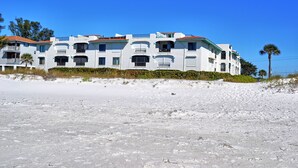 A beachfront hotel with multiple balconies, a red roof, and a sandy beach in the foreground. - Ocean Park Terrace 202 · Ocean Park 202 · Rooftop Deck · 1-Month Min (Bradenton Beach)