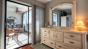 A room with a sliding glass door leading to a balcony, a large mirror, a dresser, and a table with chairs. - Ocean Park Terrace 202 · Ocean Park 202 · Rooftop Deck · 1-Month Min (Bradenton Beach)