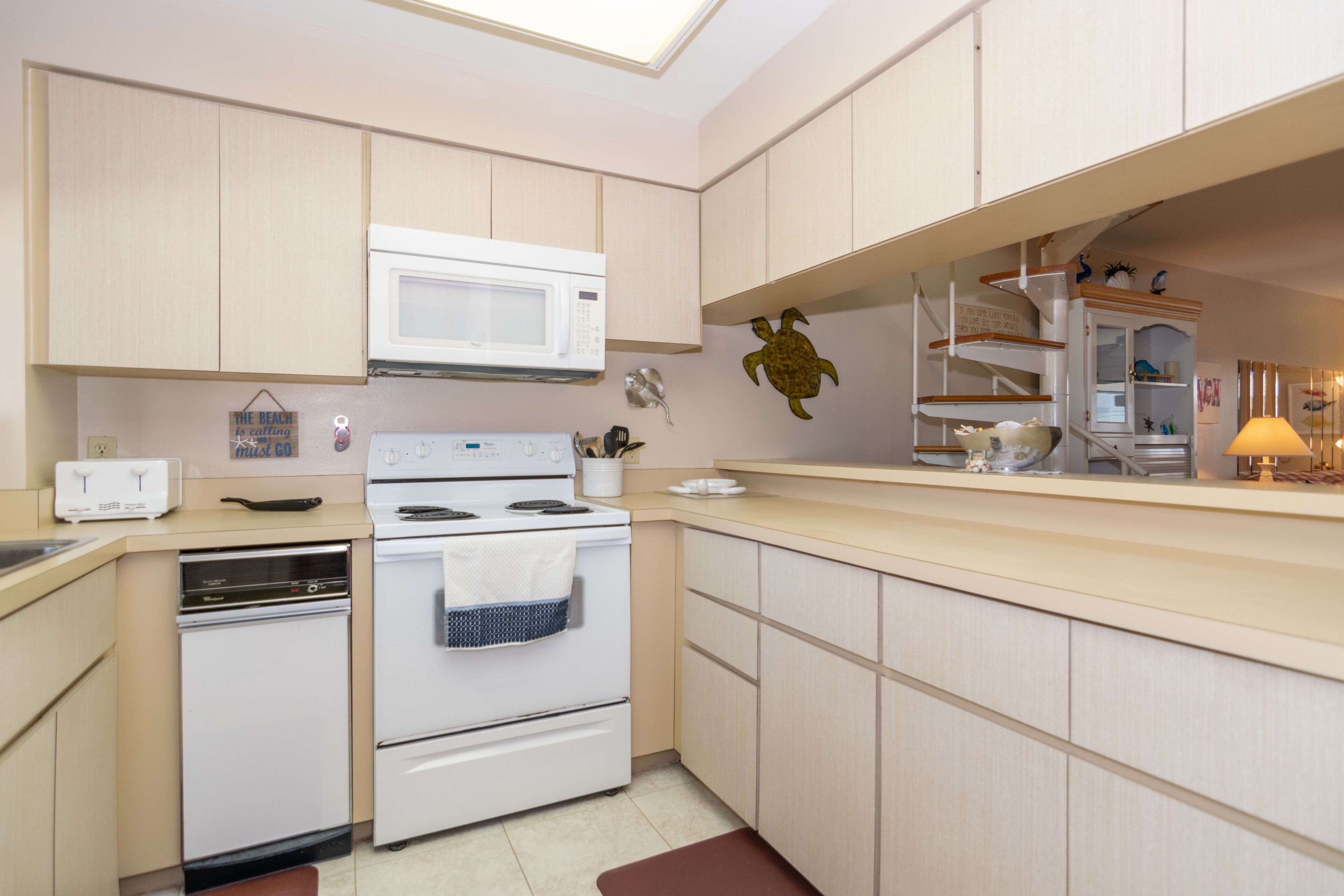 Una cocina moderna con armarios de madera clara, una estufa blanca, un microondas y una pequeña isla con un lavamanos.