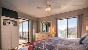 A bedroom with a large bed, a ceiling fan, a dresser, a mirror, and a balcony with a view. - Ocean Park Terrace 202 · Ocean Park 202 · Rooftop Deck · 1-Month Min (Bradenton Beach)