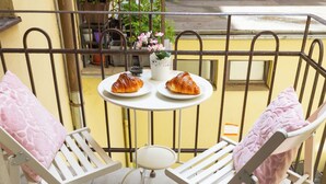A balcony with two white chairs, a small round table with two croissants, and a potted plant with pink flowers. - Dalia 3 BR, 2 BA 10 min walk from Old Town Square (Praha 1)