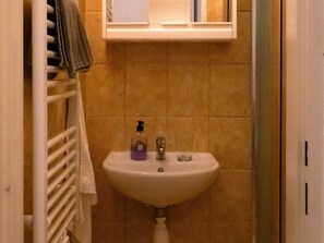 Un baño con un lavamanos blanco, un perchero y un ventanal sobre el lavamanos.