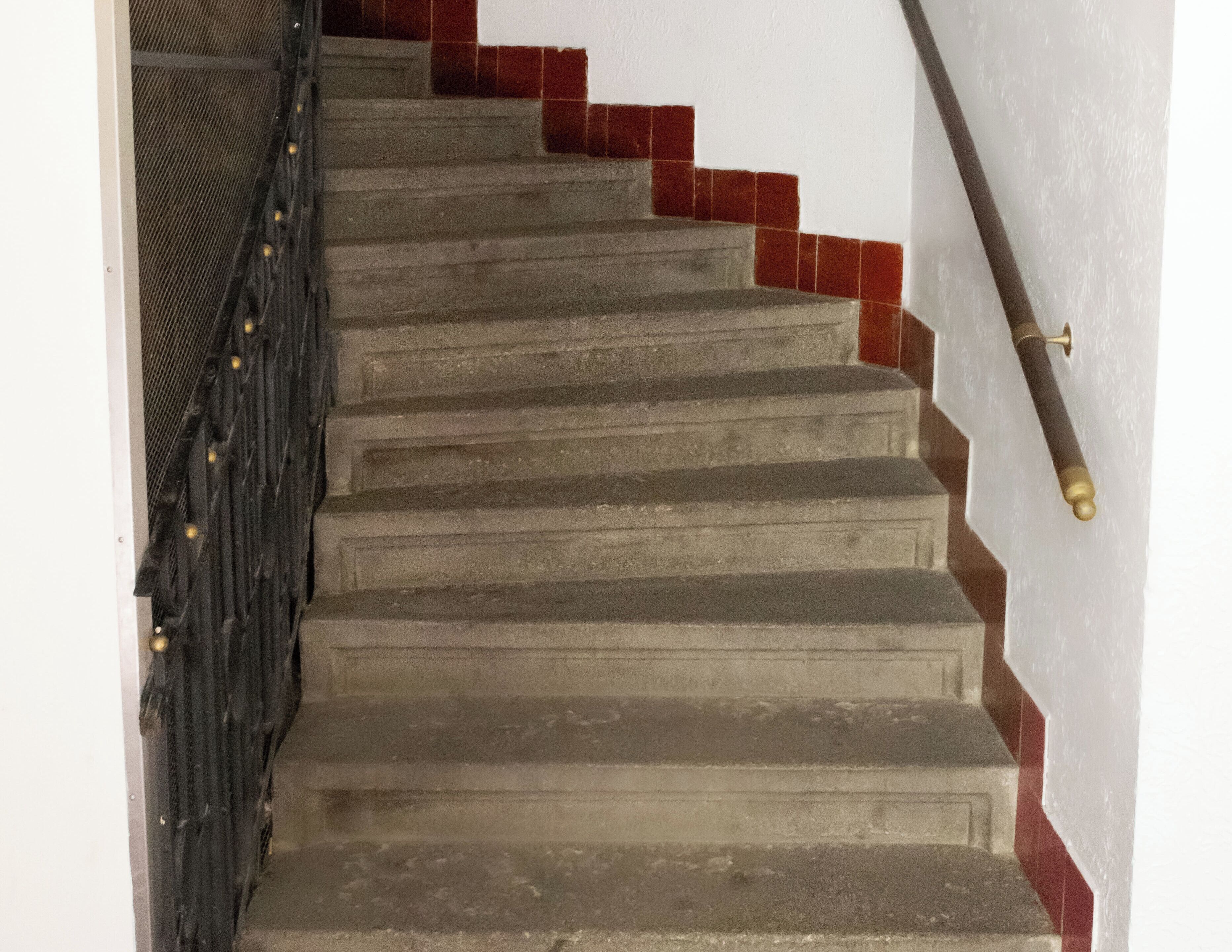 Una escalera con barandilla de metal y escalones de baldosas rojas.