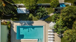 Eine Vogelperspektive zeigt einen rechteckigen Swimmingpool, umgeben von einer Poolterrasse mit Liegestühlen und Sonnenschirmen.