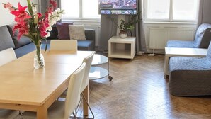 Een moderne woonkamer met een houten eettafel, een bank, een televisie op een standaard en een potplant.