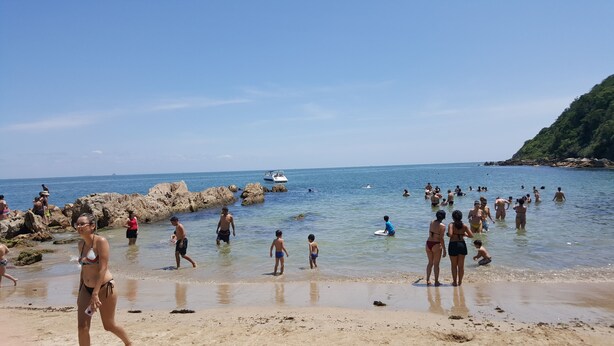Ein voller Strand mit Menschen, die im Wasser schwimmen und spazieren gehen.
