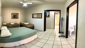 Ein Zimmer mit einem Bett, zwei Einzelbetten, einem Deckenventilator, einem Spiegel und einer Tür zu einem anderen Raum.
