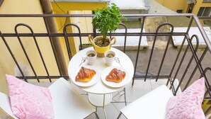 Varanda com mesa posta para dois, exibindo croissants e uma planta.