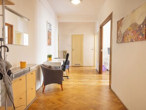 A hallway with a wooden floor, a chair, a desk, and a door.