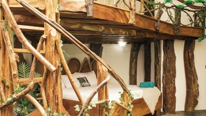 Une pièce rustique avec un escalier en bois, un lit doté d’une tête de lit blanche et un sol en pierre.
