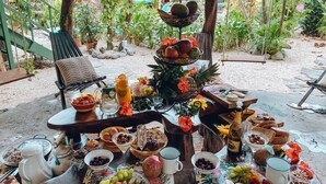 Un buffet de petit-déjeuner avec un assortiment de fruits, de viennoiseries et de boissons, disposé sur une table dans un cadre de jardin.