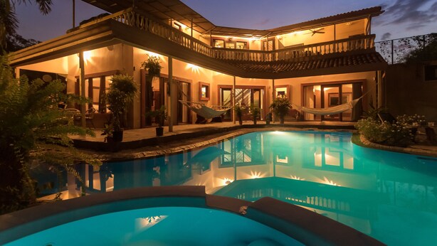 Une maison à deux étages avec une piscine, un espace salon extérieur et un hamac.