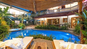 An indoor swimming pool with lounge chairs, surrounded by tropical plants and a wooden deck. - 🌴16 Bed Compound Oasis 🌴Downtown Jaco with Private Pool & Hot Tub (Jaco Beach)