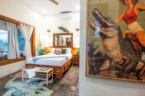 A room with a bed, a small table, a mirror, and a large painting of a crocodile.
