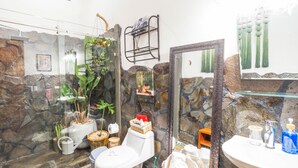 A bathroom with a stone wall, a glass shower enclosure, a toilet, a sink, and a mirror. - 🌴16 Bed Compound Oasis 🌴Downtown Jaco with Private Pool & Hot Tub (Jaco Beach)