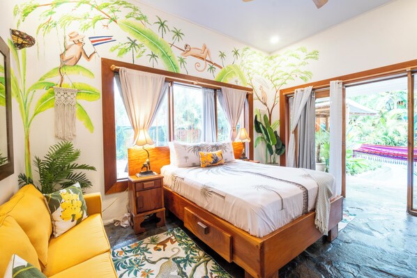 A bedroom with a bed, nightstands, a desk, and a chair. There are curtains, a window, and a view of the outdoors. - 🌴16 Bed Compound Oasis 🌴Downtown Jaco with Private Pool & Hot Tub (Jaco Beach)