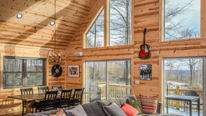 A cozy cabin interior with a dining area, a large sofa, and a guitar hanging on the wall. - Woods-stock (McHenry)