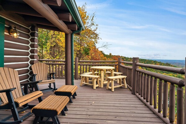 A wooden deck with picnic tables and benches, overlooking a scenic landscape.