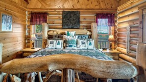 Une chambre dans une cabane en rondins, avec un lit, deux tables de chevet, une fenêtre avec des rideaux et un plafond en bois.