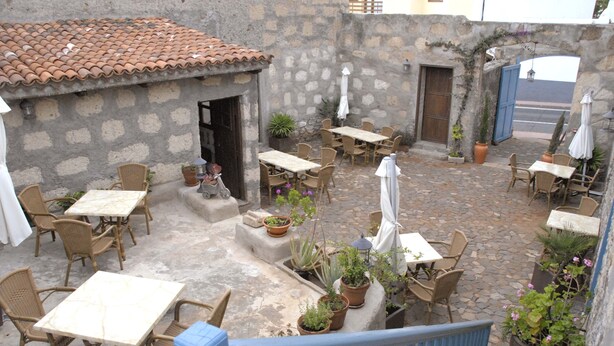 Un patio al aire libre con paredes de piedra, techo de tejas de arcilla y varias mesas y sillas.