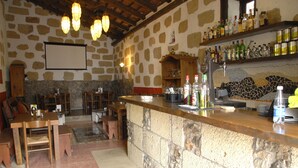 Un rústico espacio de bar con paredes de piedra, muebles de madera y una variedad de botellas y vasos en estantes.