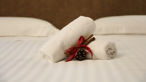 A neatly folded white towel on a bed with a pine cone and cinnamon sticks tied with a red ribbon. - Montis (San Massimo)