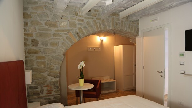 A bedroom with a stone archway, a bed, a small table with a vase, a chair, and a wardrobe. - Montis (San Massimo)