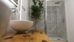 A bathroom with a wooden countertop, a white bowl, a potted plant, and a shower with patterned tiles. - Montis (San Massimo)